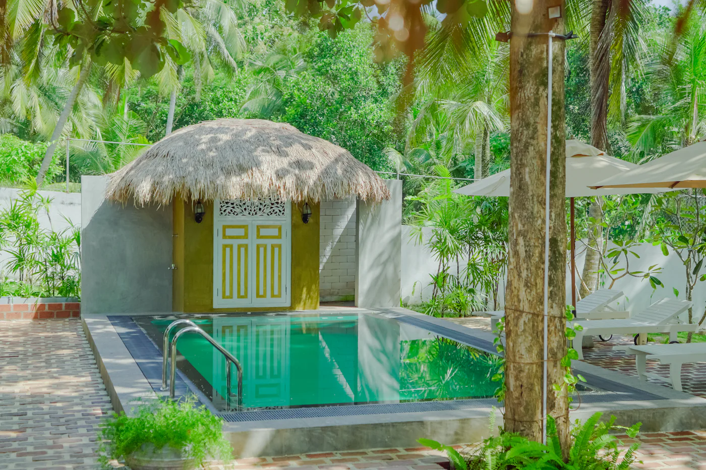 Turquoise swimming pool beside a thatched cabana framed by coconut palms